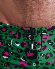 Close-up view of the CAMO CHAMELEON Swim Trunks mens swimsuit in teal with pink and black animal print with an internal drawstring cord in black showing custom branded golden buttons by BANG! clothing brand.