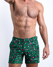 Front view of model wearing the CAMO CHAMELEON men’s beach tailored shorts in a forest green color with white and pink camo print  by the Bang! Clothes brand of men's beachwear from Miami.