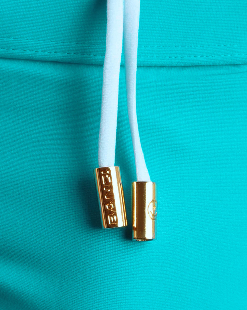 Close-up view of men’s summer swimwear by BANG! clothing brand, showing white cord with custom branded golden cord ends, and matching custom eyelet trims in gold.