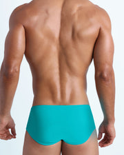 Back view of a male model wearing men’s swim sungas in azure color by the Bang! Clothes brand of men's beachwear.