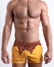 Front view of model wearing the CHOCO-BANG men’s beach shorts in a yellow color with a brown melting ice cream print around the waist by the Bang! Clothes brand of men's beachwear from Miami.