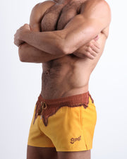 Side view of men’s shorter leg length shorts in a yellow color with brown melting graphic made by Miami based Bang brand of men's beachwear.