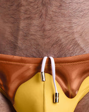 Close-up view of the CHOCO BANG men’s summer shorts by BANG! clothing brand, showing white cord with custom branded golden cord ends, and matching custom eyelet trims in gold.