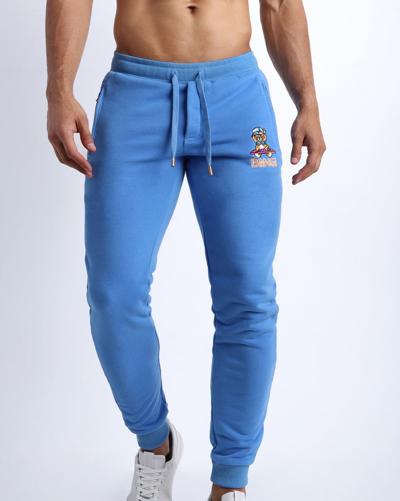 Frontal view of male model wearing the BANG! Clothes CITY BLUE Tracksuit Pants with frontal drawstring closure. This athletic jogger has an embroidered Bang! Logo with the signature Mister TJ tiger. 
