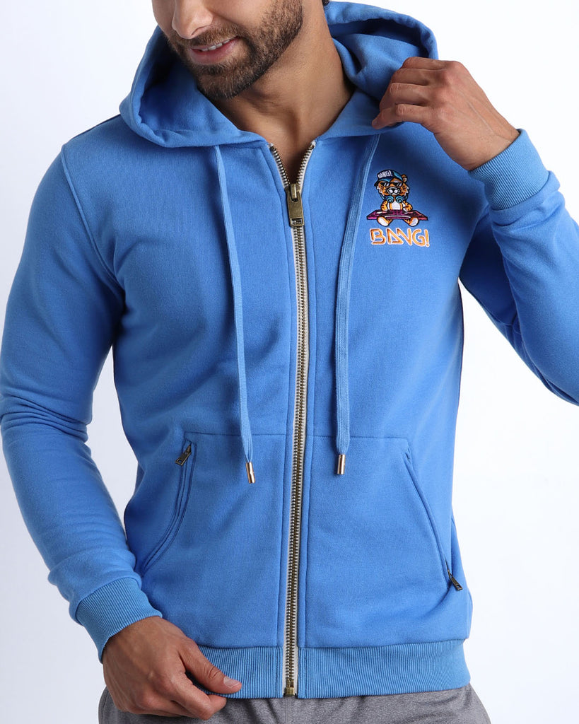 Frontal view of male model wearing the BANG! Clothes CITY BLUE Tracksuit Hoodie Jacket with frontal zipper closure. This long-sleeve jacket has an embroidered Bang! Logo with the signature Mister TJ tiger. 