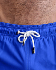 Close-up view of the CLUB BLUE men’s summer shorts, showing white cord with custom branded golden cord ends, and matching custom eyelet trims in gold.