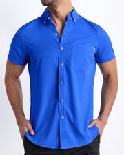 Front view of a sexy male model wearing CLUB BLUE mens short-sleeve stretch shirt in a bright blue color by the Bang! brand of men's beachwear from Miami.