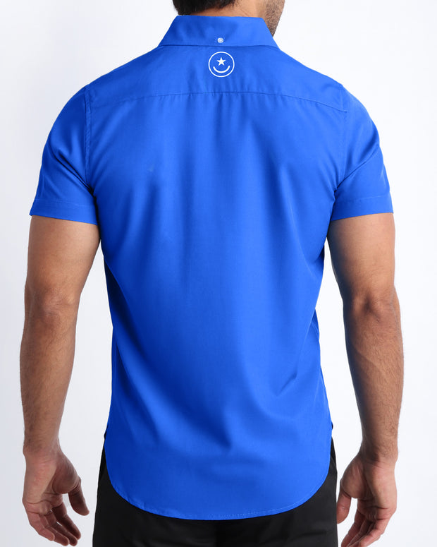 Back view of a male model wearing CLUB BLUE men’s Hawaiian shirt in a cobalt blue color by the Bang! Clothes brand of men&