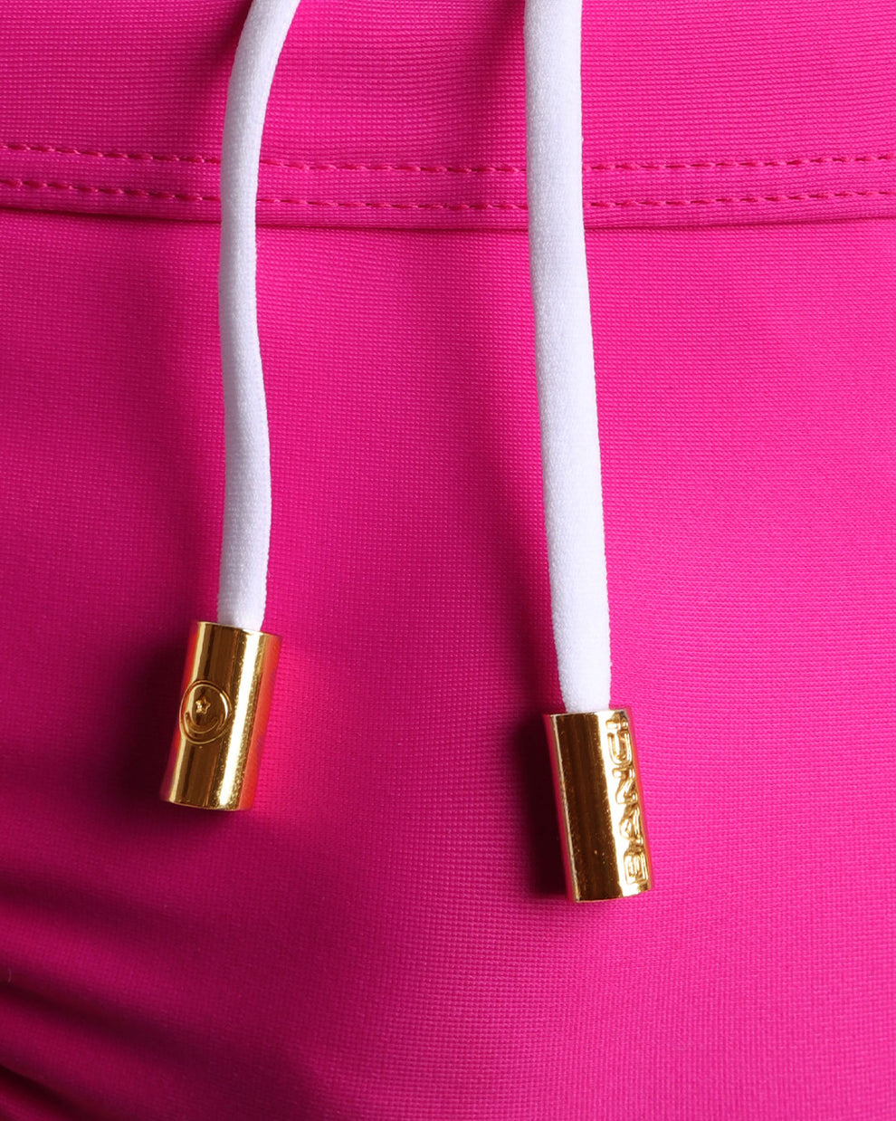 Close-up view of men’s summer swimwear by BANG! clothing brand, showing white cord with custom branded golden cord ends, and matching custom eyelet trims in gold.