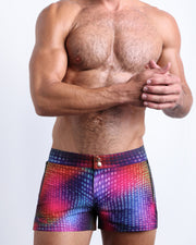 Front view of model wearing the CONFESSIONS ON A SAND FLOOR men’swim bottoms inspired by the 80s disco ball music scene in a blue, purple, yellow, green pop of color by the Bang! Clothes brand of men's beachwear from Miami.