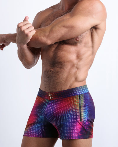 Left side view of men’s Summer swimsuit in CONFESSIONS ON A SAND FLOOR in a pop color disco ball print in purple, blue, red and yellow made by Miami based Bang brand of men's beachwear.