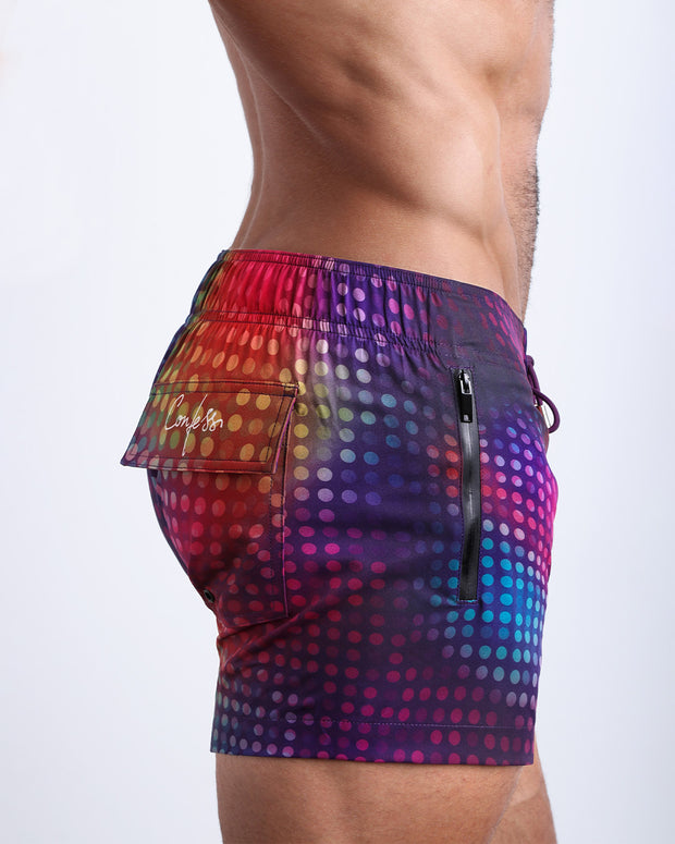 Side view of a man wearing the CONFESSIONS ON A SAND FLOOR shorter leg length swimming shorts with side zipper pocket in a disco ball print by BANG! Clothes.
