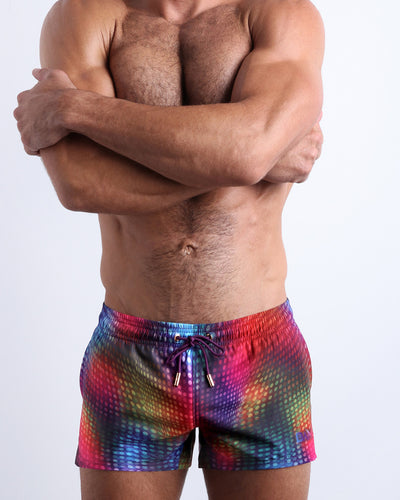 Front view of model wearing the CONFESSIONS ON A SAND FLOOR men’s beach shorts in multi colors in a disco ball print by the Bang! Clothes brand of men's beachwear from Miami.