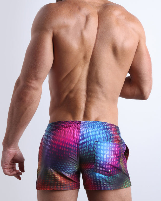 Back view of male model wearing the CONFESSIONS ON A SAND FLOOR beach trunks for men by BANG! Miami in red, purple, blue, green, orange disco ball print by Bang! Clothes based in Miami.