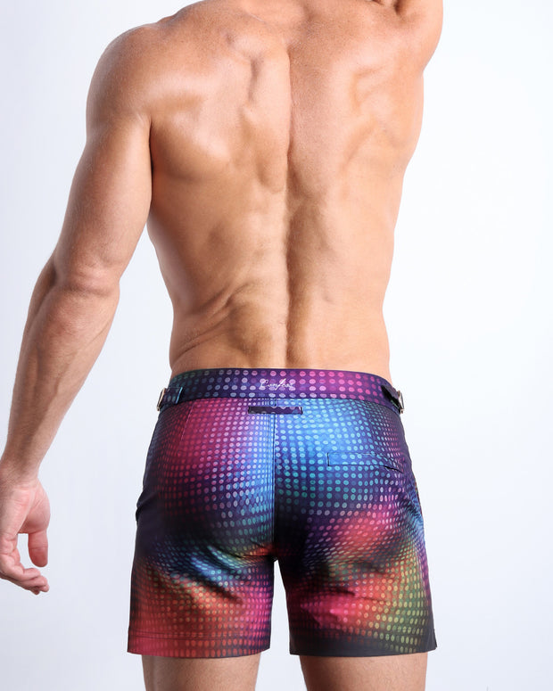 Back view of male model wearing the CONFESSIONS ON A SAND FLOOR beach trunks for men by BANG! Miami inspired by the 80s disco ball music scene in a blue, purple, yellow, green pop of color.