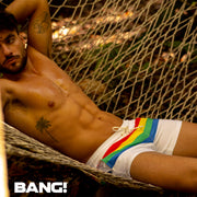 Male model laying down wearing the FOUR EVER STRIPES VOL 2 swim trunks for men in solid white with stripes in red, yellow, blue and green by Bang! Clothing of Miami.