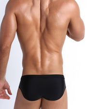 Back view of a male model wearing men’s swim brief in black by the Bang! Clothes brand of men's beachwear from Miami.