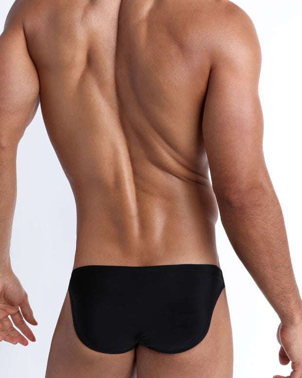 Back view of a male model wearing men’s swim mini-brief in black by the Bang! Clothes brand of men&
