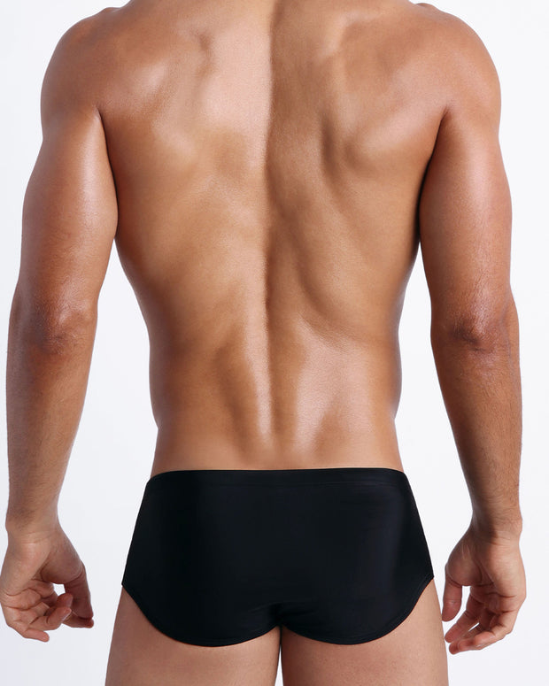 Back view of a male model wearing men’s swim sungas in black by the Bang! Clothes brand of men&
