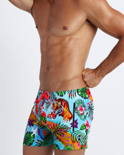 Left side view of a sexy male model wearing a jungle print premium mens swimming shorts for the beach with zipper pocket.