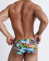 Back view of a model wearing men's bikini style swimwear in a light blue with a jungle print by Bang! Clothes.