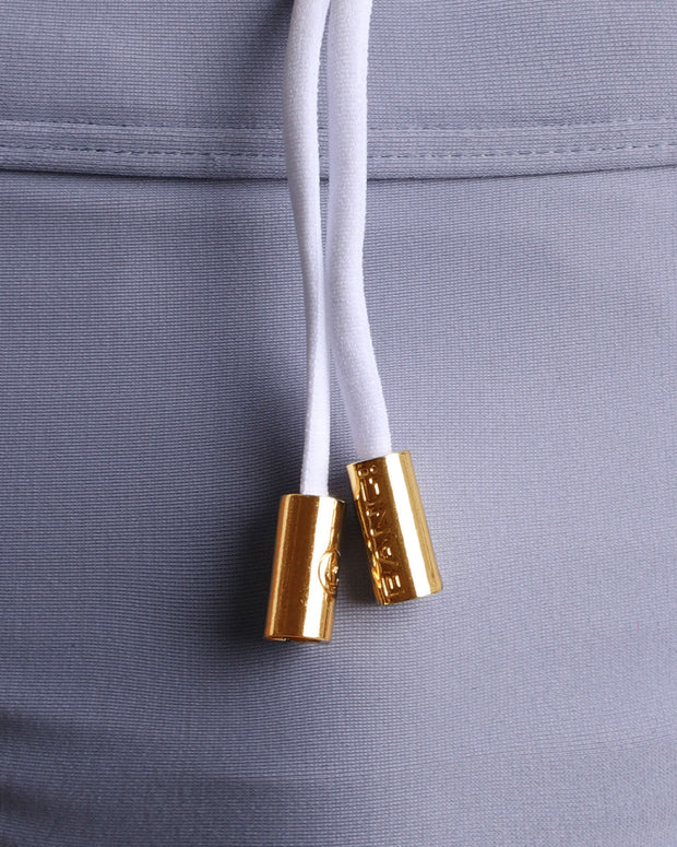 Close-up view of men’s summer swimwear by BANG! clothing brand, showing white cord with custom branded golden cord ends, and matching custom eyelet trims in gold.