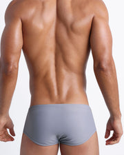 Back view of a male model wearing men’s swim sungas in stone grey color by the Bang! Clothes brand of men's beachwear.