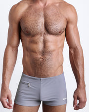 Frontal view of a sexy male model wearing men’s swimsuit with mini pockets in grey color by the Bang! Menswear brand from Miami.