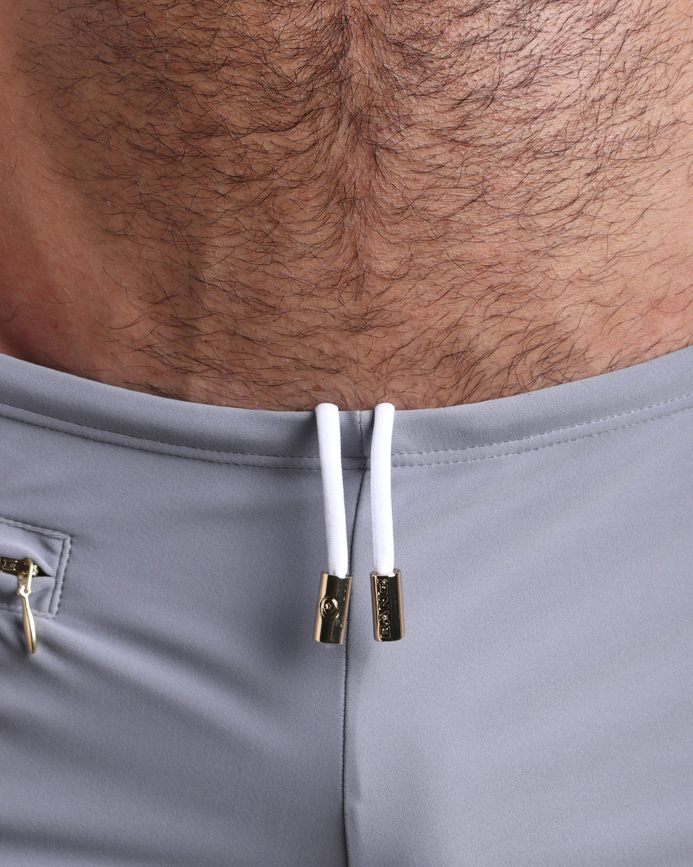 Close-up view of the GREY ANATOMY Swim Sunga mens swimsuit a grey color with white internal drawstring cord showing custom branded golden buttons by BANG! clothing brand.