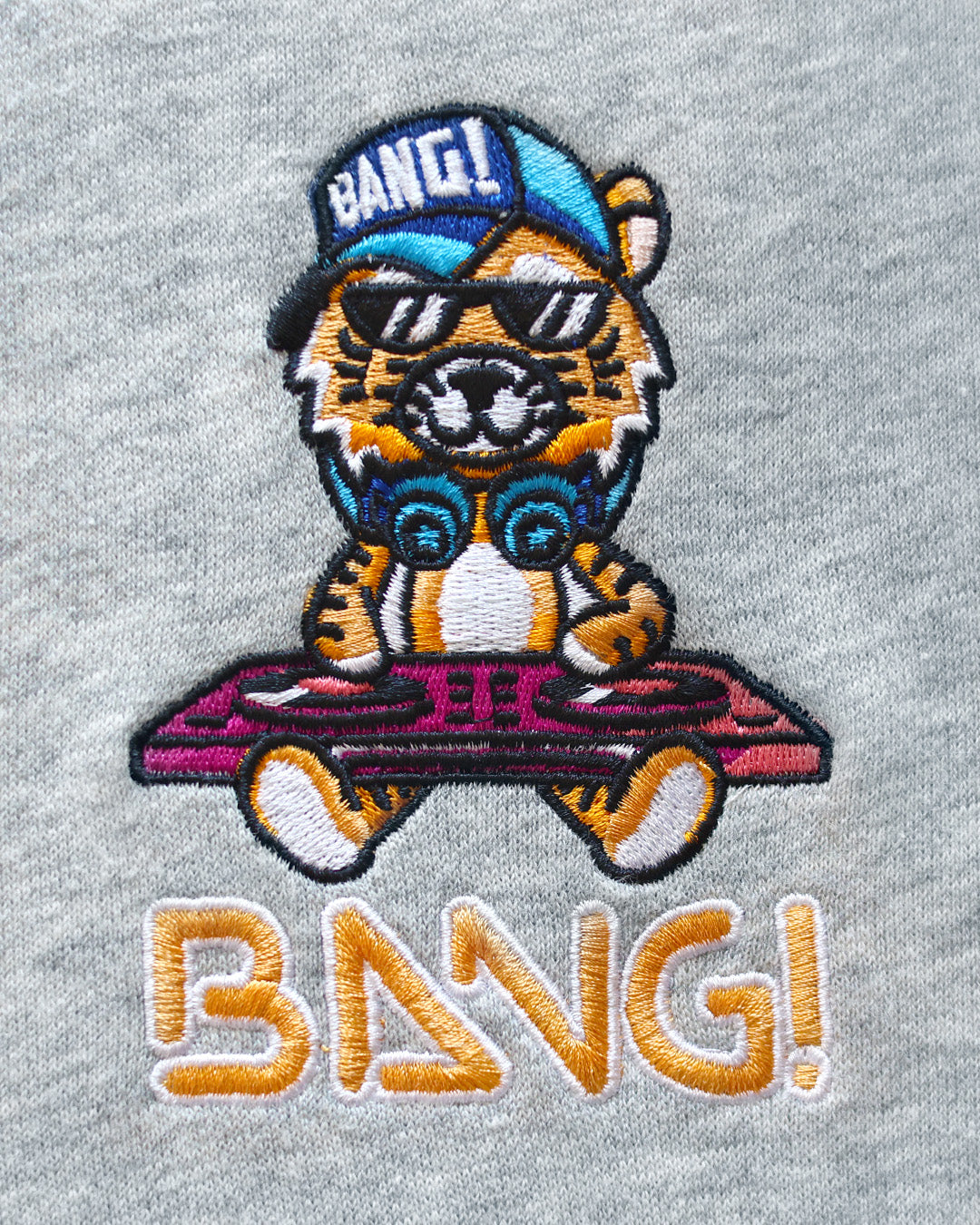 Close-up image of the embroidered BANG! Logo featuring the brands signature MISTER TJ character with clubbing and disc-jockey details in bright colors.