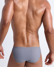 Back view of a male model wearing men’s swim mini-brief in stone color by the Bang! Clothes brand of men's beachwear.