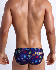 Back view of model wearing the HEY MISTER TJ (CLUB MIX) Men’s beach briefs by BANG! with clubbing and disc-jockey details in dark colors.