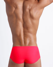 Back view of a sexy male model wearing men’s swim sungas in neon red by the Bang! Clothes brand of men's beachwear.