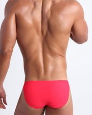 Back view of a male model wearing men’s swim mini-brief in neon red by the Bang! Clothes brand of men's beachwear.