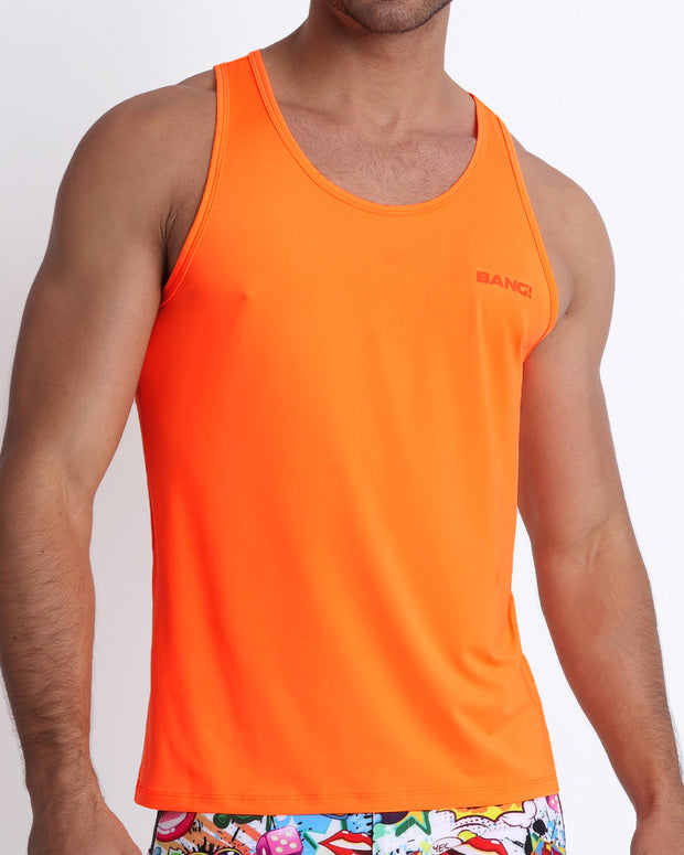 Frontal view of a sexy male model wearing a men’s tank top in a beautiful orange color by the Bang! Menswear brand from Miami.