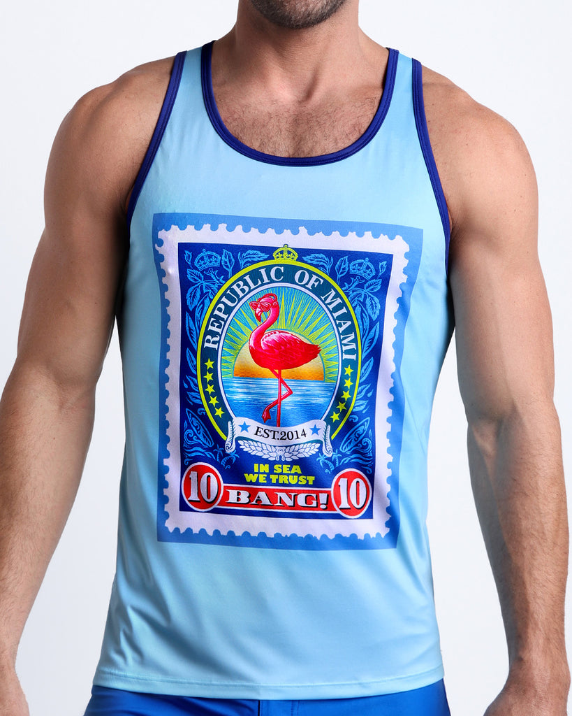 Front view of model wearing the IN SUN WE TRUST men’s beach tank top in a light sky blue color and a Miami flamingo pop art postage stamp on the chest by the Bang! Clothes brand of men's beachwear from Miami.