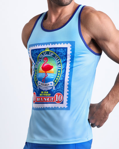 Side view of men’s casual tank top in IN SUN WE TRUST featuring a light blue color and a hot pink flamingo pop art postage stamp made by Miami based Bang brand of men's beachwear.