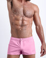 Frontal view of a sexy male model wearing the LA BEACH EN ROSE men’s square leg swim trunks in a solid light pink color by the Bang! Menswear brand from Miami.