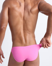 Back view of a male model wearing men’s swim mini-brief in light rose pink by the Bang! Clothes brand of men's beachwear.