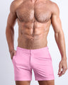 Frontal view of a sexy male model wearing the men’s LA BEACH EN ROSE beach tailored shorts in a light pink color by the Bang! Menswear brand from Miami.