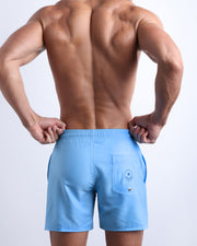 Back view of male model wearing the MAGNET BLUE beach trunks for men by BANG! Miami in a sky blue color with a back pocket.