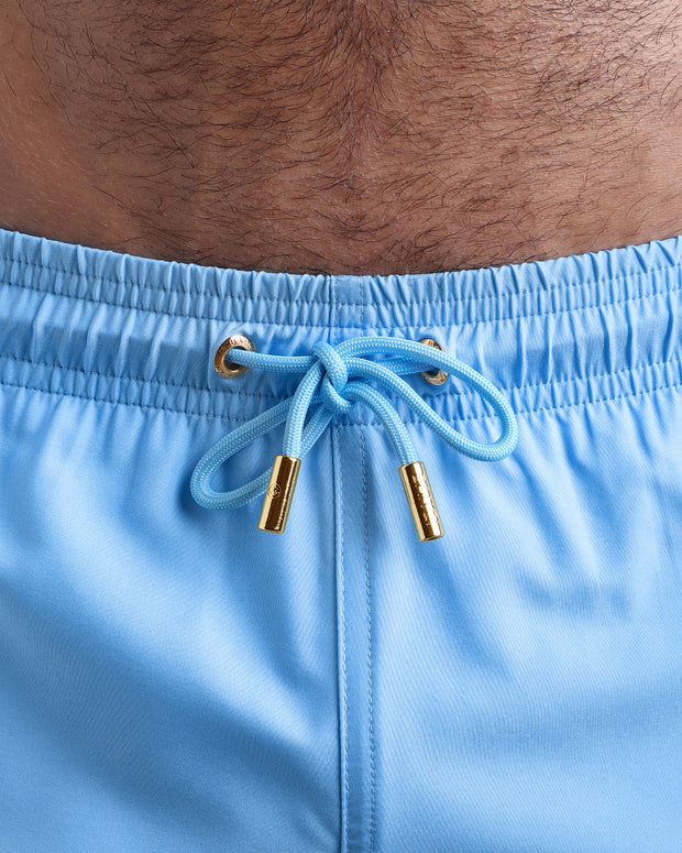 Close-up view of the MAGNET BLUE men’s summer shorts, showing light blue cord with custom branded golden cord ends, and matching custom eyelet trims in gold.