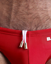 Close-up view of the MAJESTIC RED men’s drawstring briefs showing white cord with custom branded golden cord ends, and matching custom eyelet trims in gold.