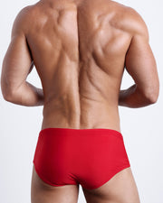 Back view of a male model wearing men’s MAJESTIC RED swim sungas in a red color by the Bang! Clothes brand of men's beachwear.