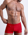 Frontal view of a sexy male model wearing men’s swimsuit with mini pockets in a bright red color by the Bang! Menswear brand from Miami.