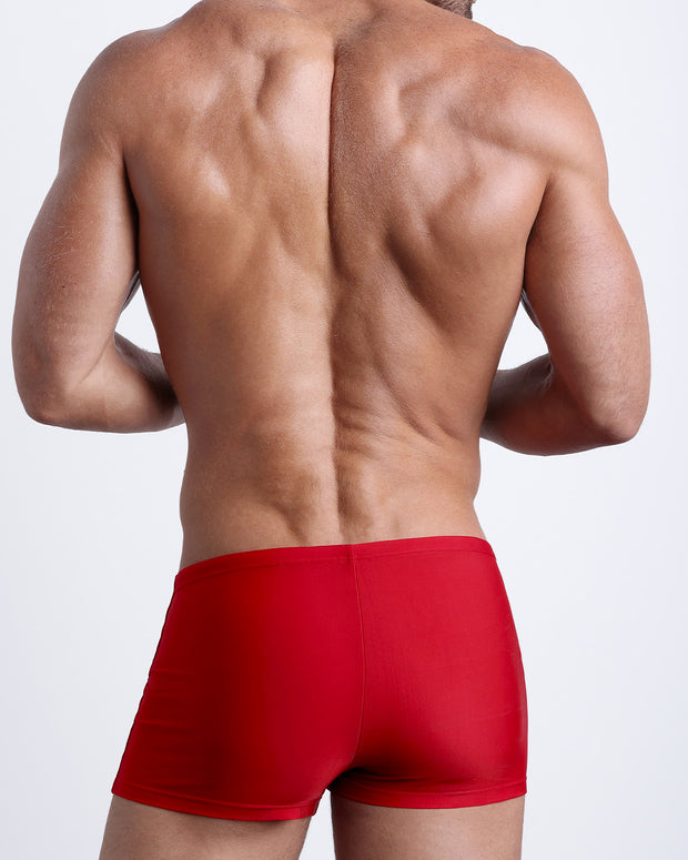 Back view of a male model wearing the MAJESTIC RED men’s swim trunks in a solid red color by the Bang! Clothes brand of men&