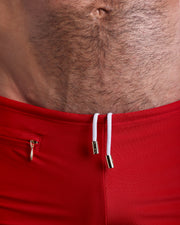 Close-up view of the MAJESTIC RED Swim Trunks mens swimsuit a true red color with white internal drawstring cord showing custom branded golden buttons by BANG! clothing brand.
