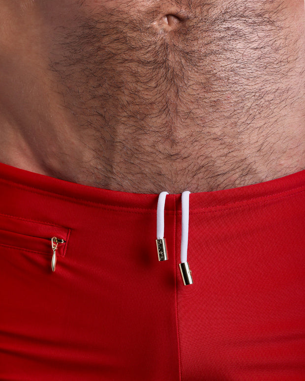 Close-up view of the MAJESTIC RED Swim Trunks mens swimsuit a true red color with white internal drawstring cord showing custom branded golden buttons by BANG! clothing brand.
