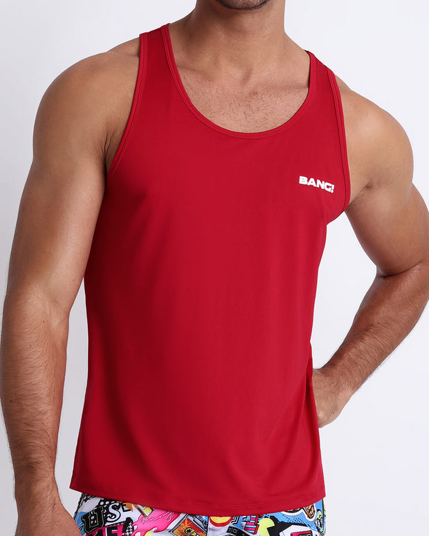 Frontal view of a sexy male model wearing a men’s tank top in red by the Bang! Menswear brand from Miami.