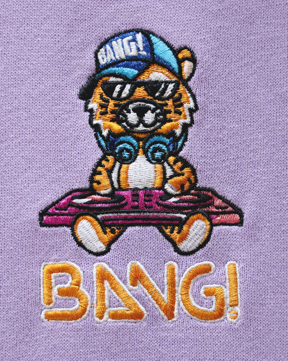 Close-up image of the embroidered BANG! Logo featuring the brands signature MISTER TJ character with clubbing and disc-jockey details in bright colors.
